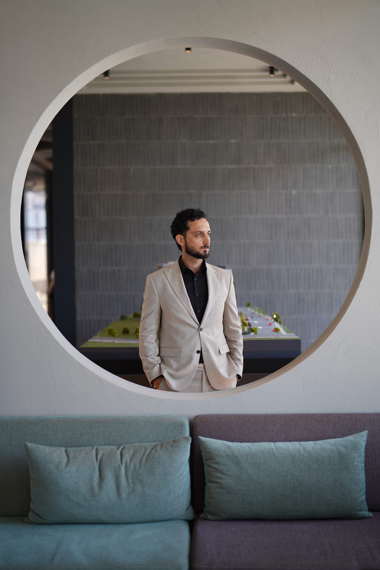 Erfan Naji framed in a circular opening, a scale model of a development behind him